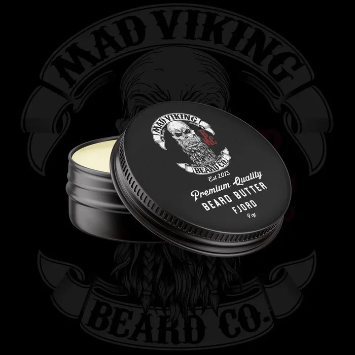 Open tin of Mad Viking premium quality beard butter, Fjord scent, with black lid, cream-colored balm, and rugged Viking logo on dark background.