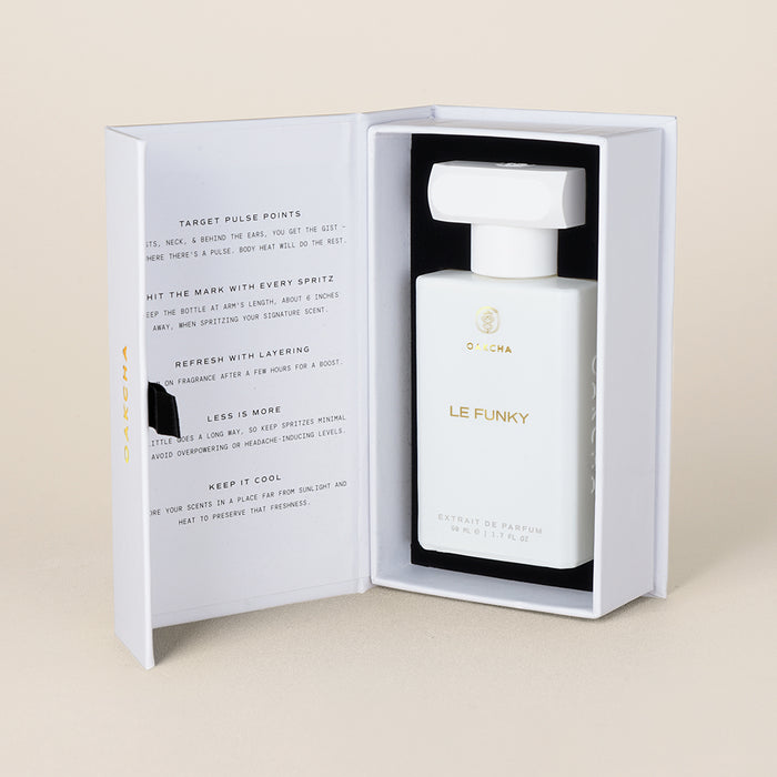Front view of Le Funky perfume in white rectangular bottle with gold logo inside open white box on beige background