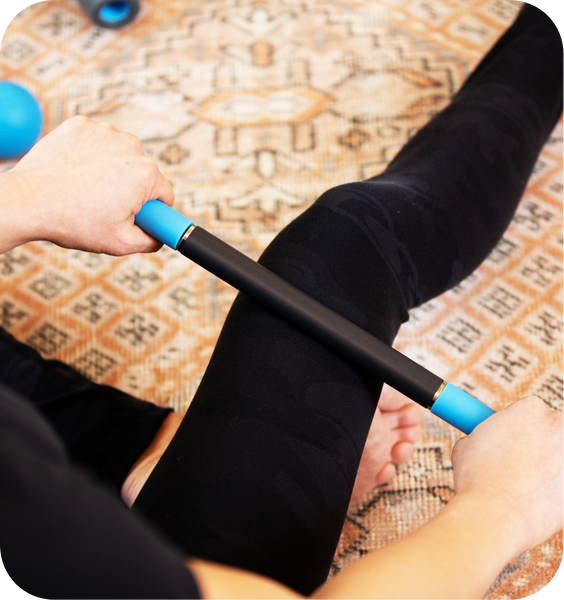 Person using a RAD ROD | RAD massage tool on their calf while sitting on a patterned carpet, promoting muscle recovery and wellness.
